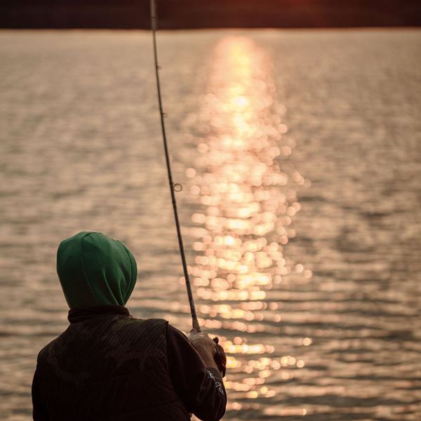 Silhouette of a person meditating during sunrise over a calm lake.